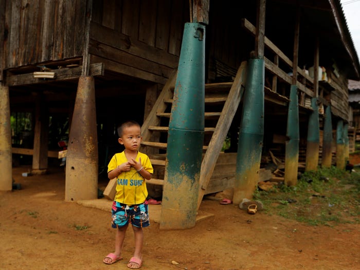 Một cậu bé đứng trước ngôi nhà được xây dựng trên bom do máy bay của Không quân Mỹ ném xuống trong Chiến tranh Việt Nam, ở làng Ban Napia, tỉnh Xiêng Khoảng, Lào